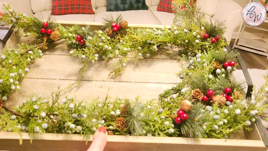 Rectangle wood tray with a jasper fir garland inside and picks with pine, pinecones, & red berries.