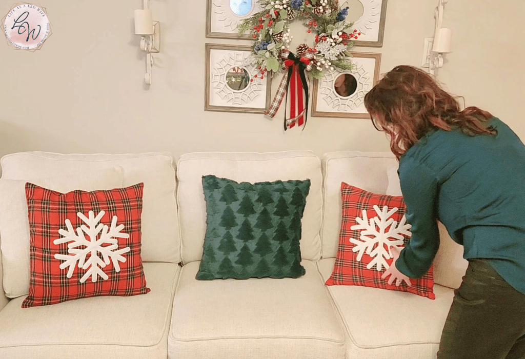 Placing a plaid pillow with a white snowflake on the couch with a wreath hung on a decorative mirror set above the it.