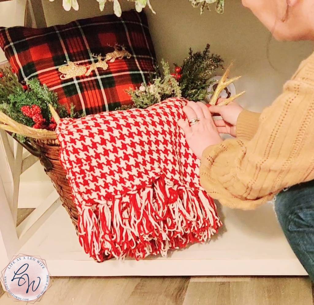 Placing an antler decor piece under a blanket inside a basket on the bottom of the faux Christmas mantle.