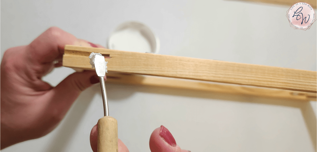 Filling the holes of a wood frame with spackle.