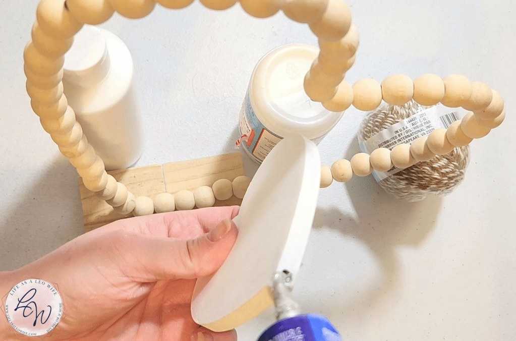 Adding Quick Grip to the bottom of a white wood heart to place in front of the wood bead heart glued to the base of the Valentine's Day shelf sitter decoration.