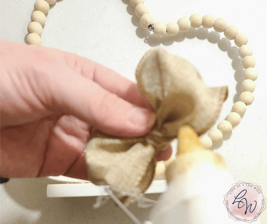 Adding hot glue to the back of the 2-loop bow to glue on the base of the Valentine's Day heart shelf sitter decoration.