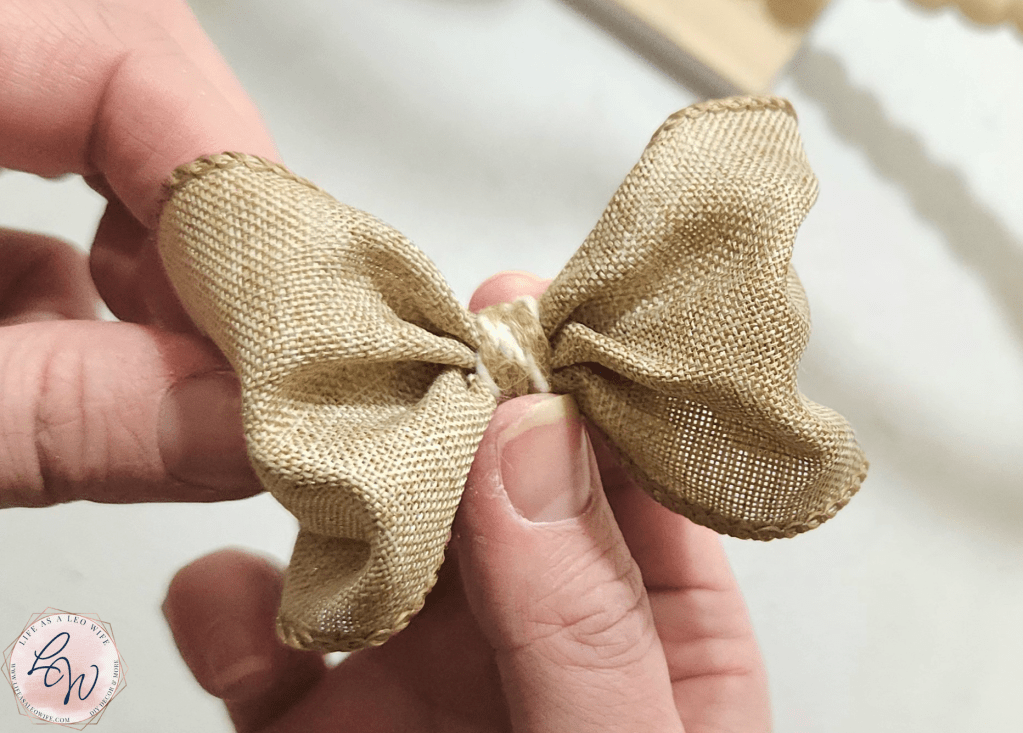 A small two-loop bow without tails with khaki and white twine wrapped around the pipe cleaner that secures the bow.