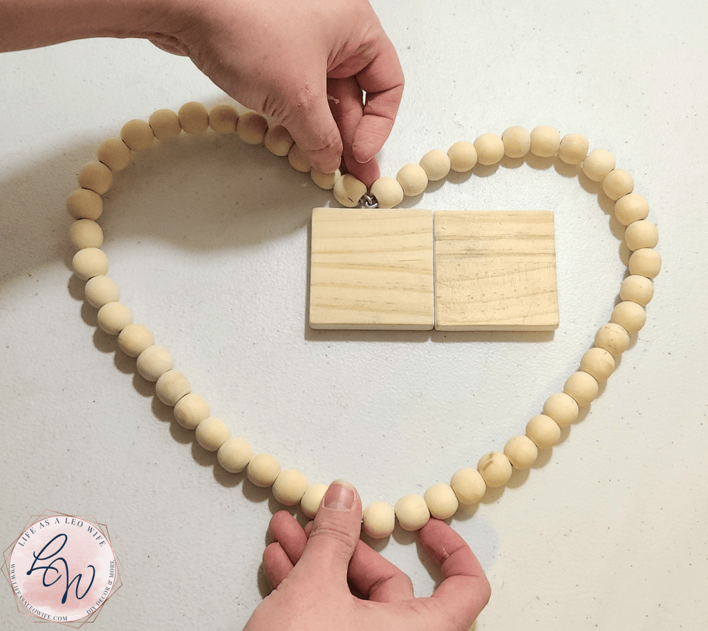Bending a round wood bead wreath into a heart shape to create a Valentine's Day shelf sitter decoration.
