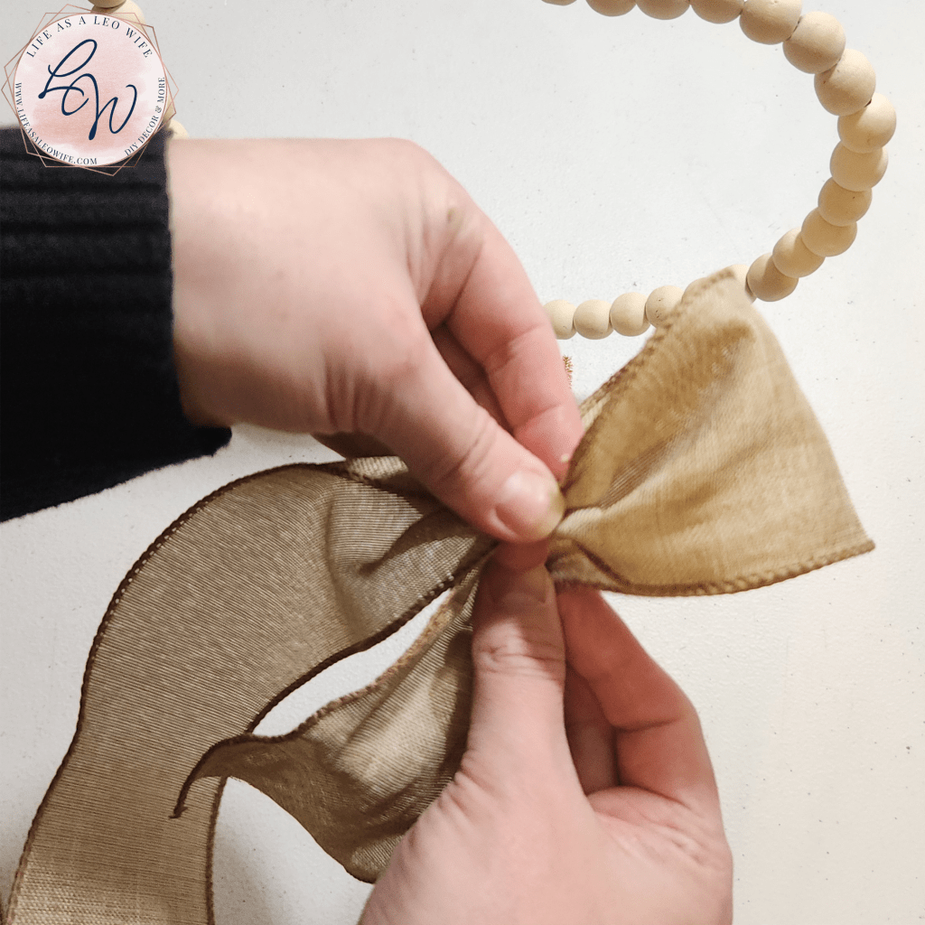Making a simple two-loop bow with khaki linen ribbon to place at the top of the Valentine's Day wood bead heart shelf sitter decoration.