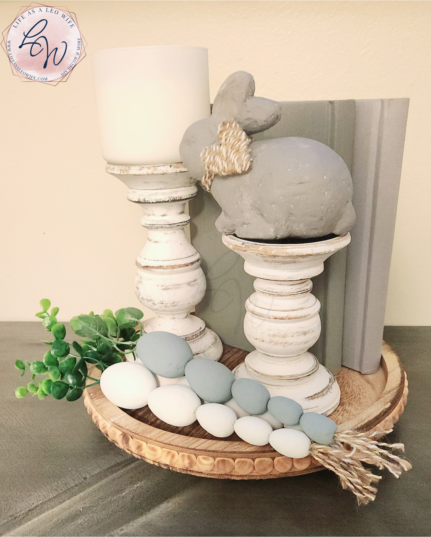Easter egg carrots laying on a farmhouse wood tray with 2 candlestick holders, a bunny, & 2 decorative books.
