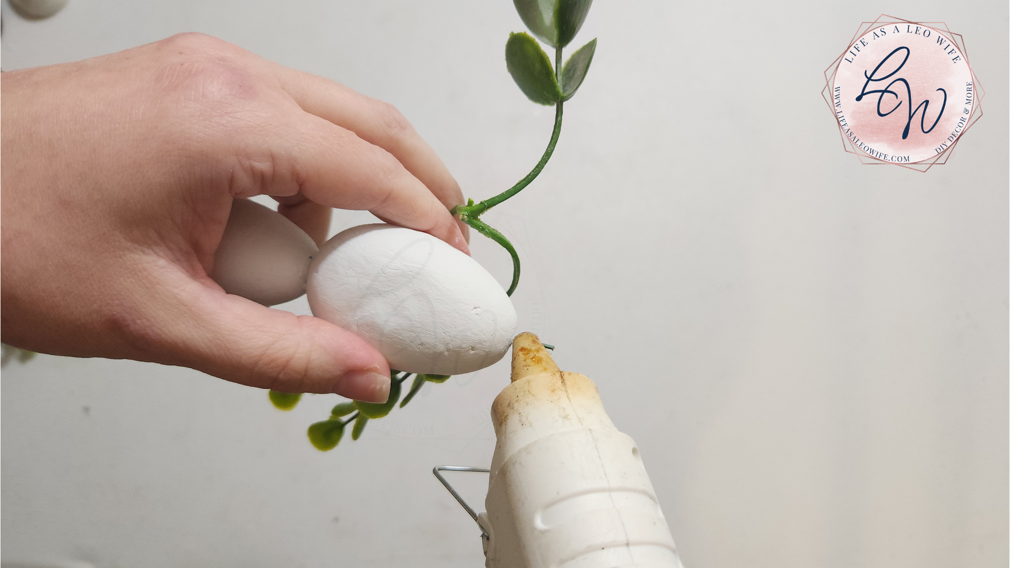 Putting hot glue on the wire on top of the DIY Easter egg carrot to attach the greenery.