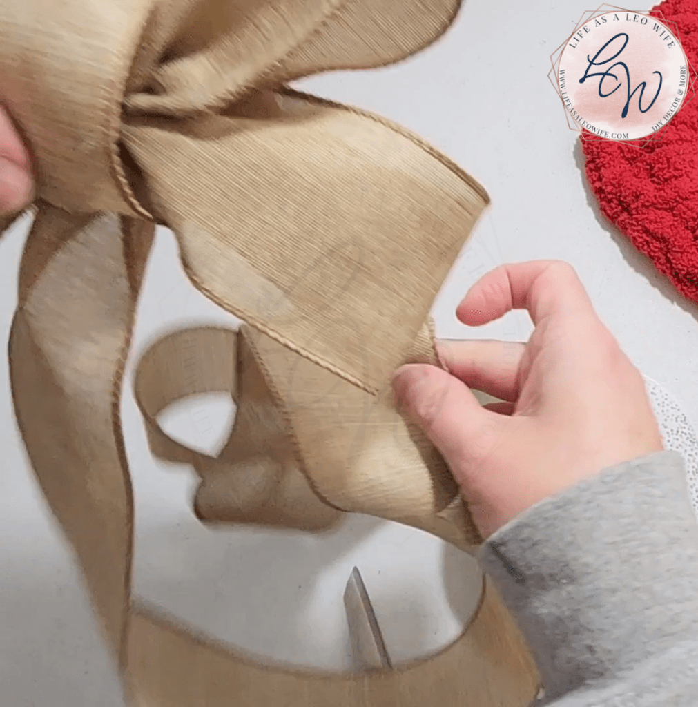 Pulling the ribbon back up to the center to form tails on the easy DIY bow.