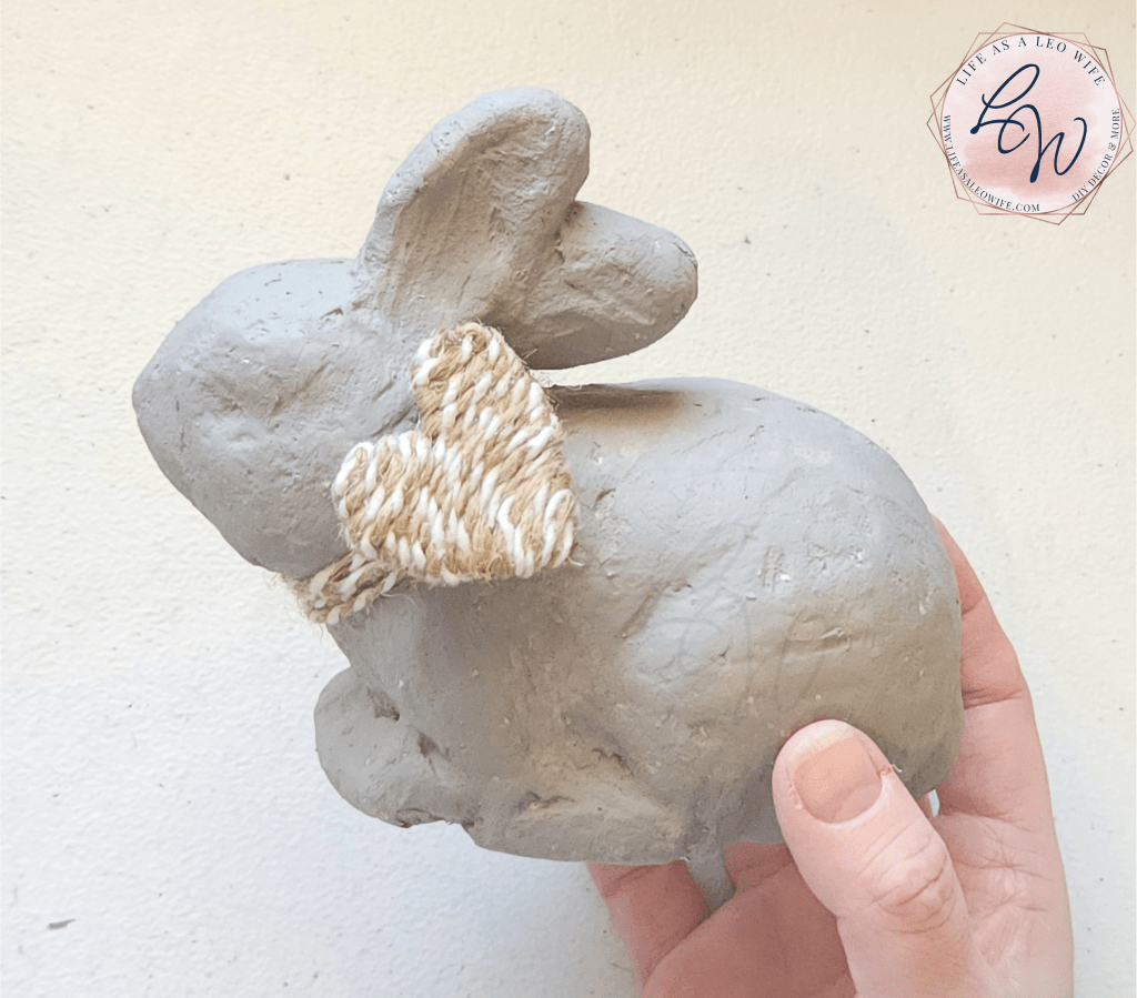 Finished DIY faux concrete bunny with khaki and white twine wrapped around the neck and a twine heart attached to it.