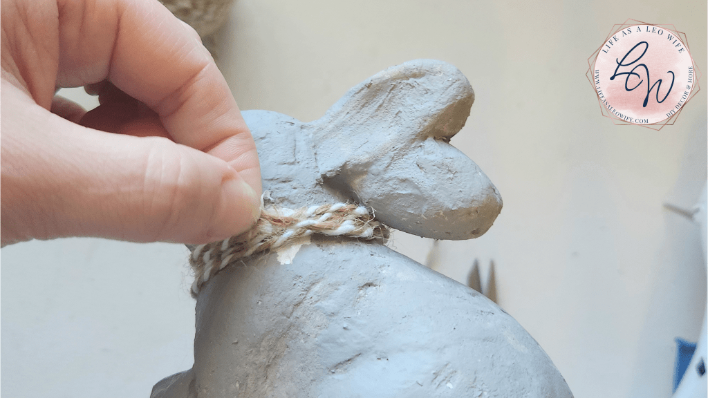 Pinching the 2 ends of the glued twine together around the neck of the DIY faux concrete bunny,