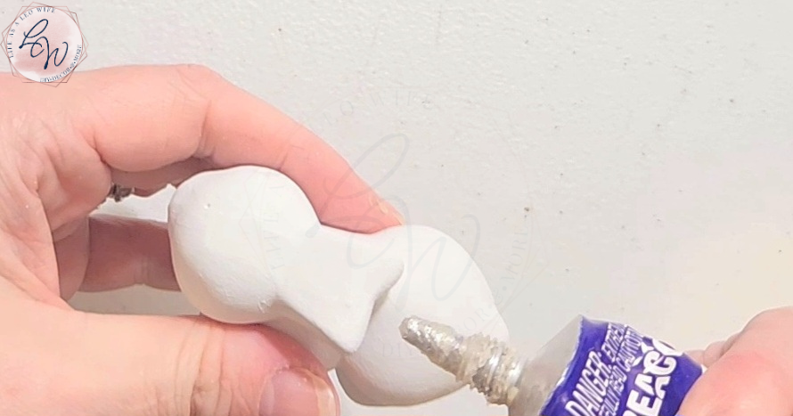 Squeezing Quick Grip on the back of a ceramic Dollar Tree bunny to glue a terracotta flowerpot to it to create a spring DIY flower holder.