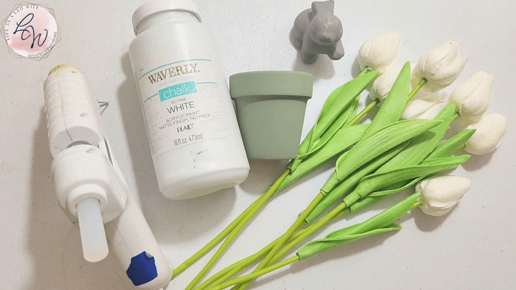 Supplies for a DIY spring bunny flowerpot: small terracotta pot and ceramic bunny from Dollar Tree, tulips, white chalk paint, and hot glue.