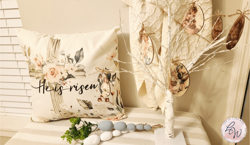A bench in the entryway with a "He is risen" pillow and lighted tree with eggs hanging from it on the top shelf and other Easter and spring decor on the bottom two shelves.