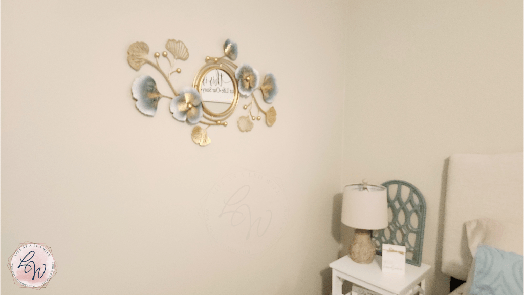 Gold metal mirror wall art decor piece with blue flowers hung on the left side of the master bedroom.