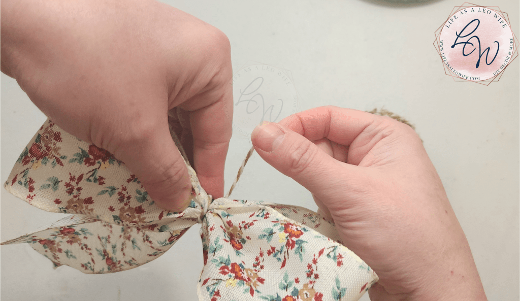 Wrapping twine around the pipe cleaner securing the bow for the embroidery hoop pocket wreath.