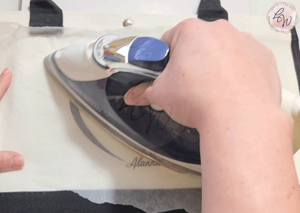 Ironing the grandmother vinyl design on a canvas tote bag to create a personalized gift.