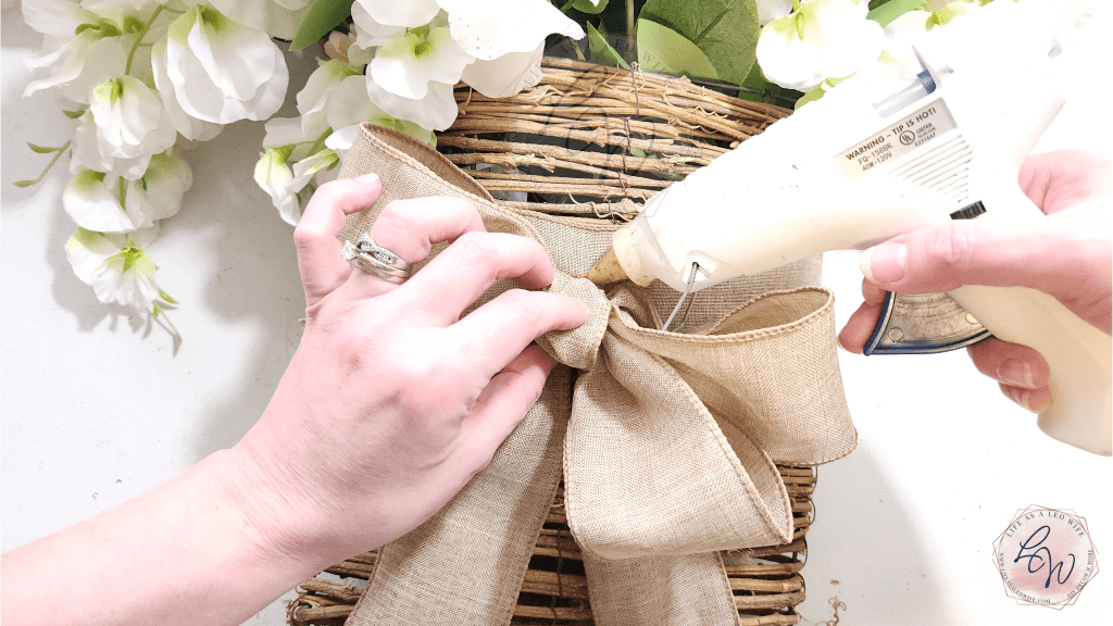 Hot gluing a bow to the front of the floral door basket.